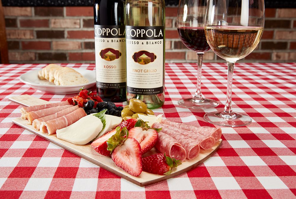 A charcuterie board with glasses and bottles of wine on a red checkered table cloth