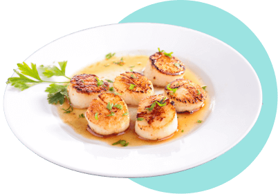 A white plate filled with seared scallops and a butter sauce with parsley