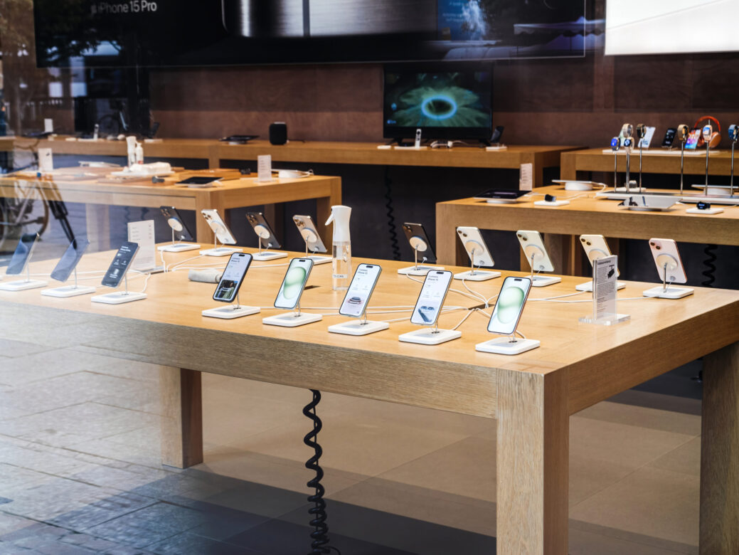 A wooden table within an Apple Store is adorned with a diverse range of Apple computers and iPhones