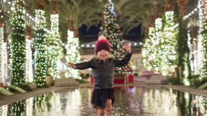 Child running across a reflective pool in front of a Christmas tree at Scottsdale Quarter