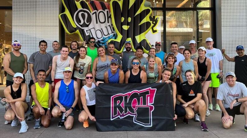 group of people in athletic clothes posing with banner that says Riot and pool floaties that say 10k tour.
