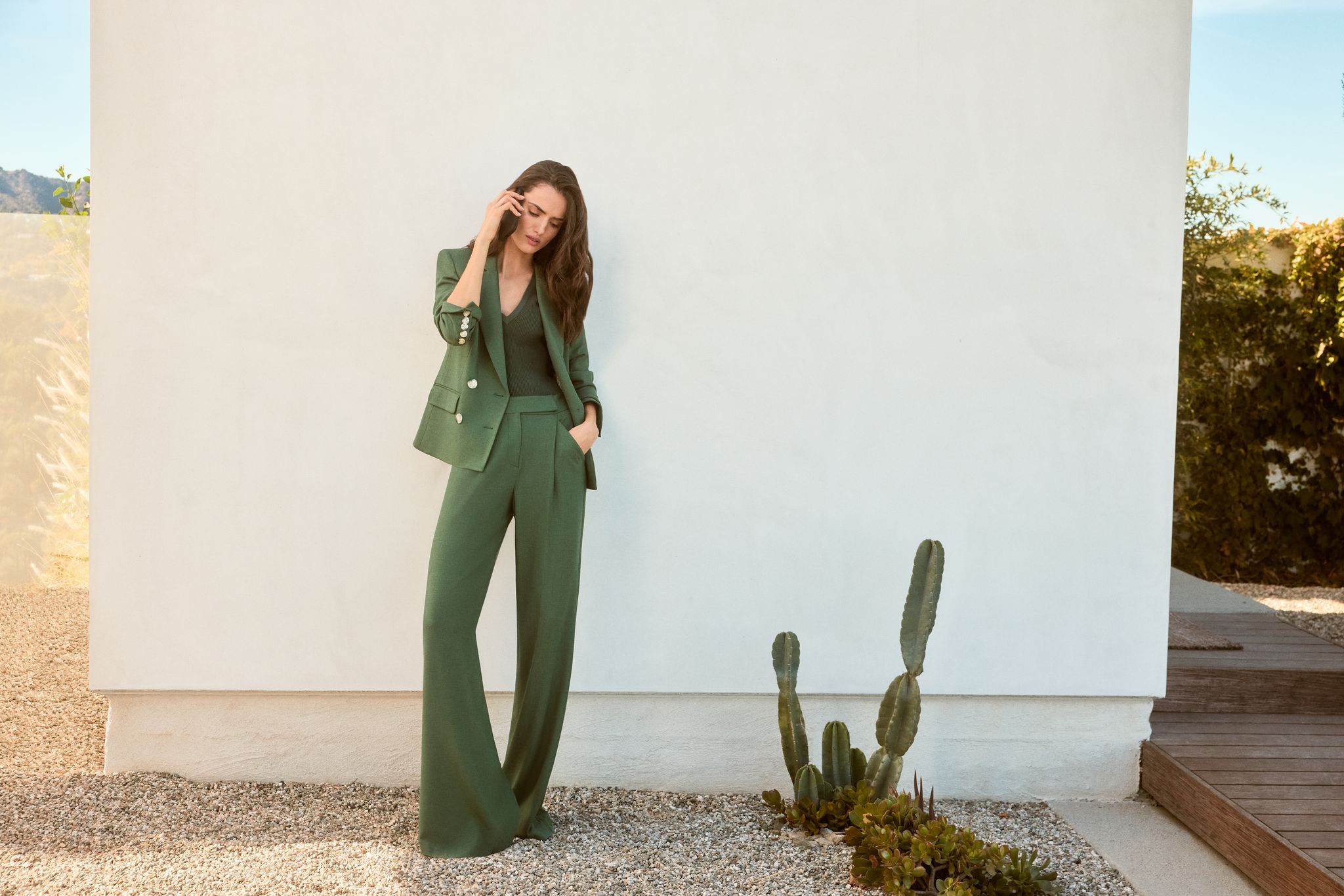 Woman in a green pantsuit standing in front of a wall, next to a cactus