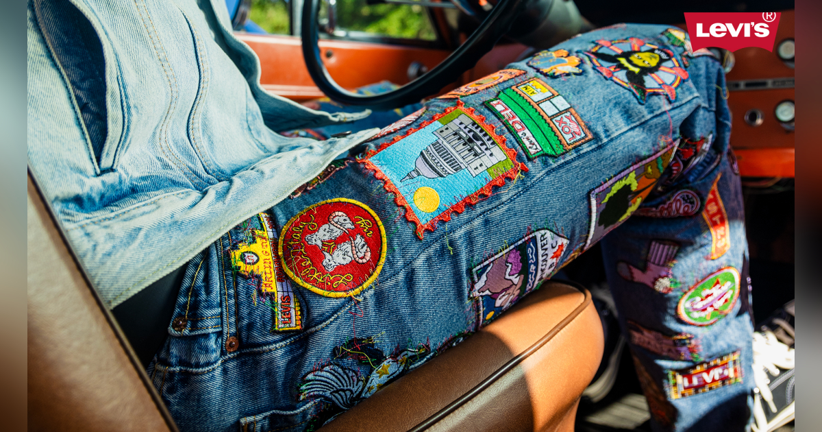 Close-up view of the leg of a person driving, wearing jeans that are full of colorful patches