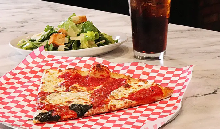A slice of pizza, side salad, and a soda