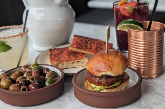 Assorted drinks, olives, bread, and a slider, on a white marble table