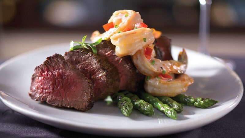 A plate of steak medallions, topped with shrimp, atop a bed of asparagus