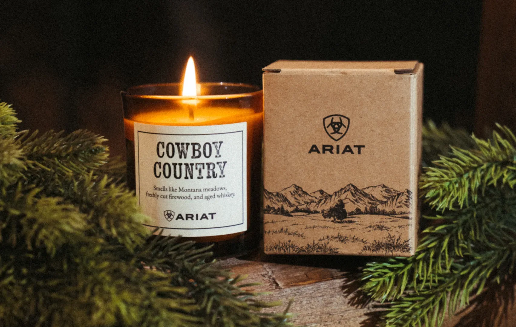 A lit Cowboy Country Candle with pine branches