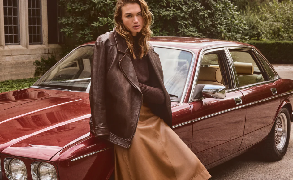 a woman leaning on a classic car in a leather jacket