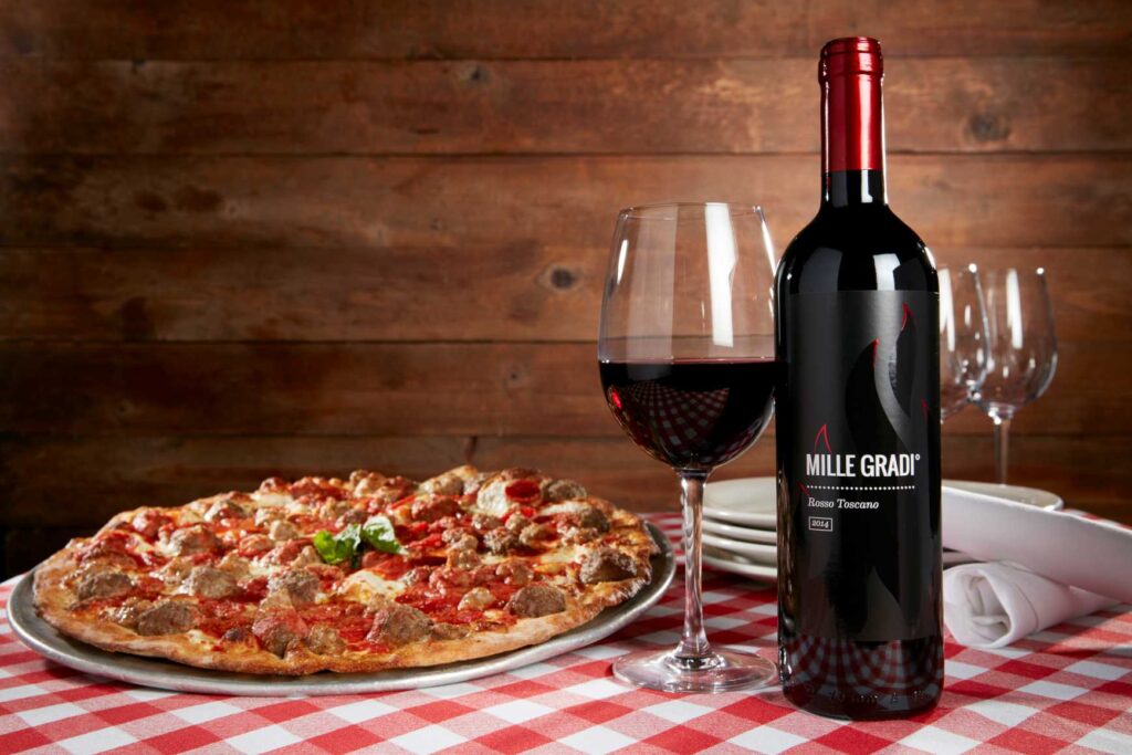 A pizza and a bottle of red wine on a table with 2 glasses